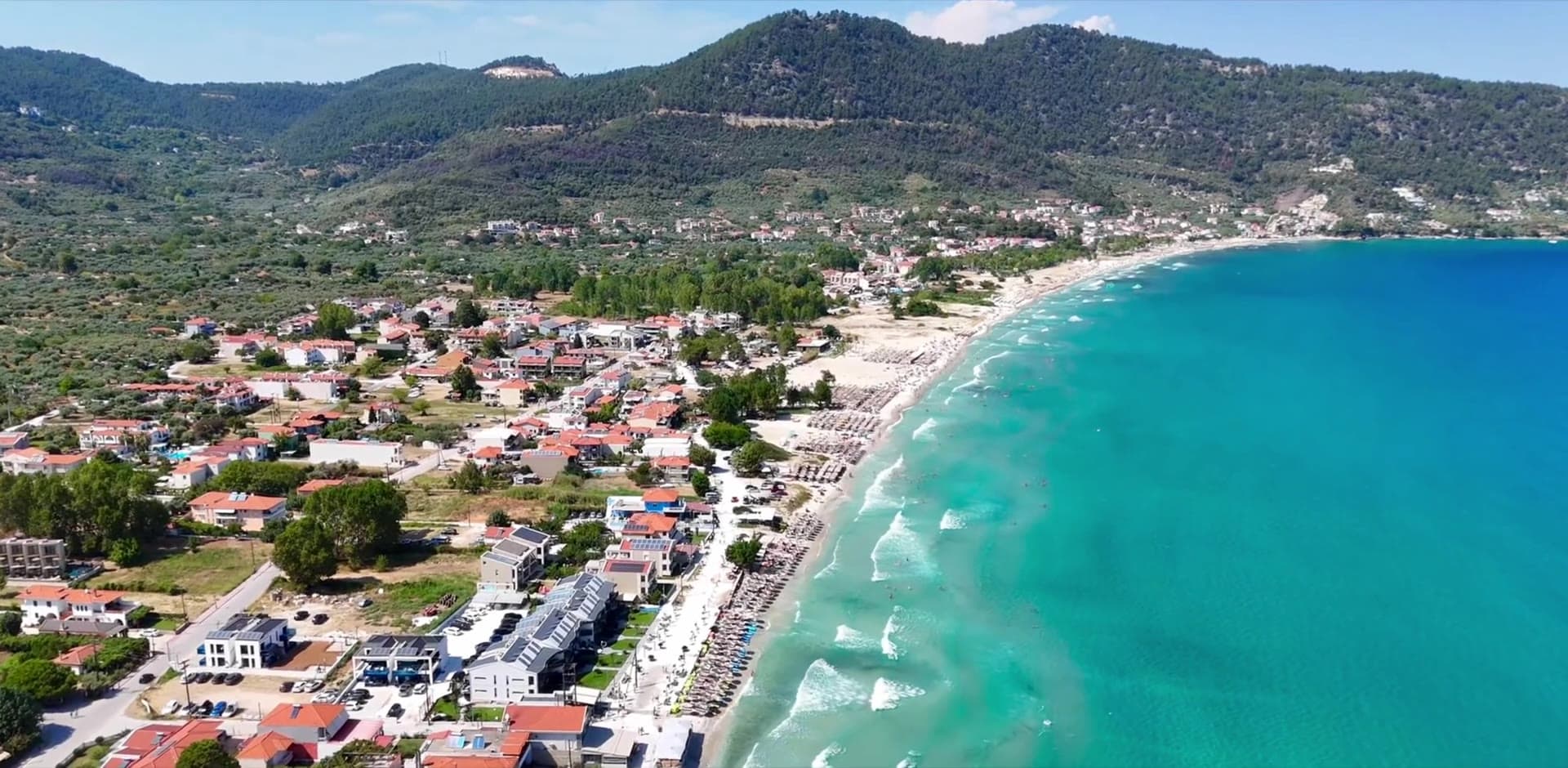 Aerial view of Golden Beach, Thassos, with the sea on the right and wooded hills behind.